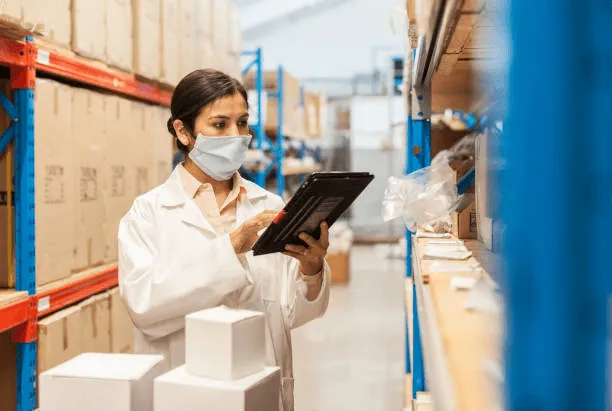Préparatrice vérifiant un stock de produits médicaux sur tablette dans un entrepôt